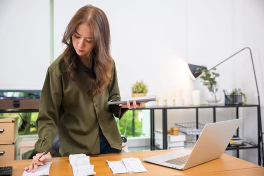 Asian female calculating family budget financial and accounting at home, young woman working with financial data calculator with tablet computer and writing make note calculate, pay bills tax online