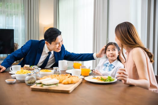 Asian family father, mother with children daughter eating breakfast food on dining table kitchen in mornings together at home before father left for work, happy couple family