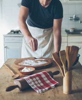 Chef making food on kitchen table. Baker man baking homemade bread dough on vintage wooden board. Retro style image. People cooking in home concept.
