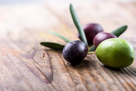 Fresh olive fruit and olive leaves on rustic wooden table background.