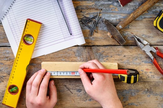 Carpenter working with crafting tools in his workshop. Top view of man's hands measuring on working desk.