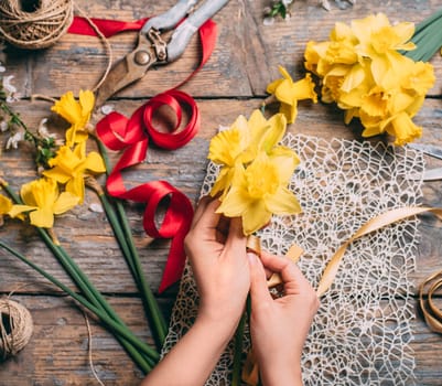 Top view of florist hands making flower bouquet with narcissus and decorative ribbon.