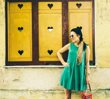 Beautiful modern young woman in fashion clothes on the street. Stylish fashionable lady smiling in front of yellow wall.