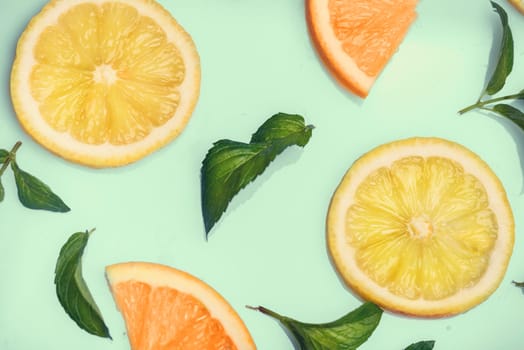 Citrus slices and mint herbs pattern on retro mint background from above. Top view of orange and lemon fruit slices on pastel background.