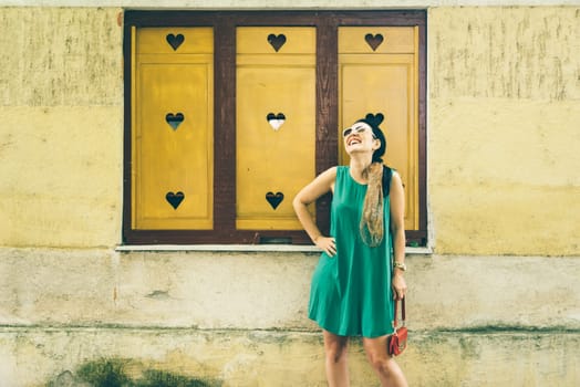 Beautiful modern young woman in fashion clothes on the street. Stylish fashionable lady smiling in front of yellow wall.