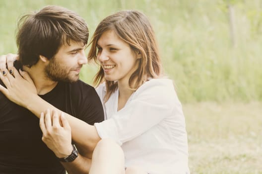 Happy loving couple hugging in nature. Portrait of young attractive smiling man and woman relaxing in green forest on sunny day. Retro filter.