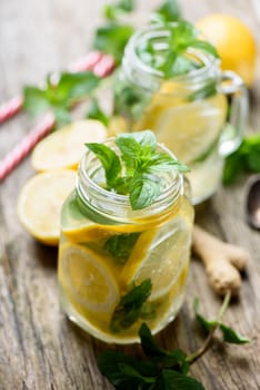 Mint lemonade refreshment beverage in retro mason jars on rustic wooden table. Gignger, lemon and herbs ingredients for summer detox drink recipe.