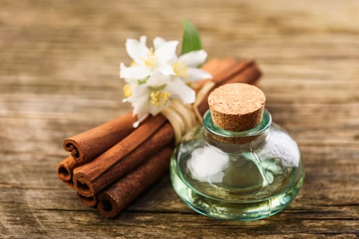 Essential massage oil with jasmine flower and cinnamon aroma on rustic wooden background. Natural spa and wellness aromatherapy treatment still life.