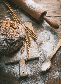 Still life with homemade baked bread, flour, wheat ears and kitchen utensils on rustic wooden table. Making organic bread on vintage kitchen table. Top view.
