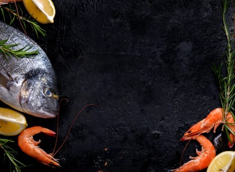 Top view of fresh sea food on grunge textured black background. Shrimps, bream, herbs, lemon and ice on slate with copyspace.