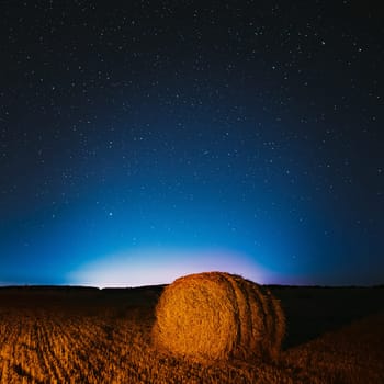 Night Starry Sky Above Haystacks In Summer Agricultural Field. Night Stars Above Rural Landscape With Hay Bales After Harvest. Agricultural Concept.