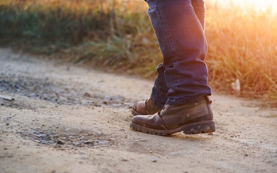 Closeup of man in hiking shoes walking on rural path in the mountain at sunset