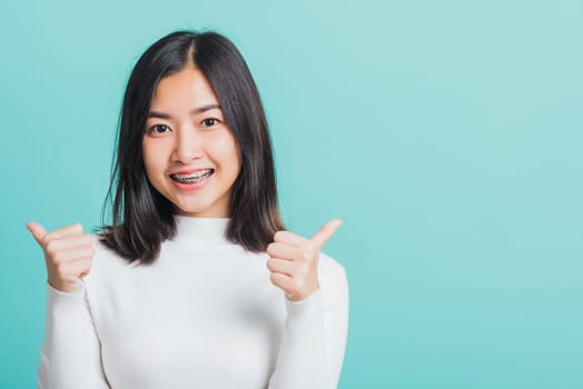 Young beautiful Asian woman cheerful smiling showing finger thumb up, Portrait happy female using showing like the gesture for good sign, studio shot isolated on a blue background