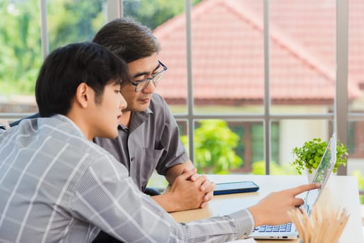 Asian young man teaching senior father how to use a modern laptop computer together in the living room at home, Son helping Dad to use the laptop for web application online