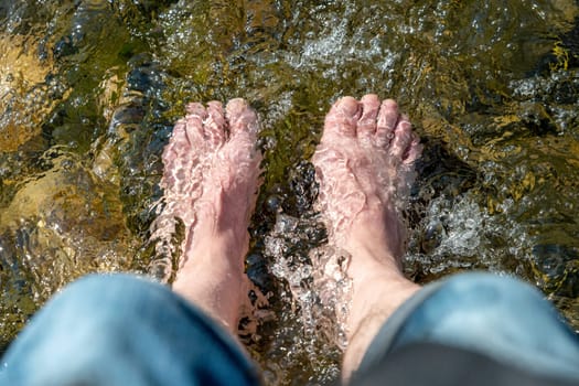 Flowing water between stones laps a man's feet in the sunshine in the summer