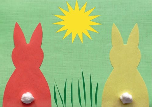 One red and one yellow paper bunny on green background with illustrated sun and grass
