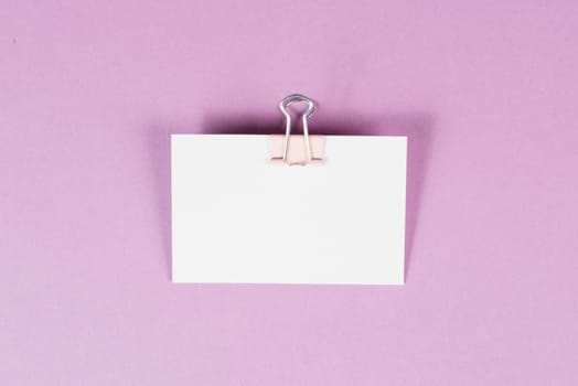 Blank white paper with a paperclip on a pink colored background, copy space for text, reminder or message in the office, communication concept