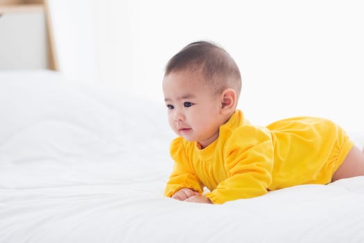 Portrait of beautiful young Asian newborn little baby prone on the bed at home, Happy baby smile wears a yellow shirt relaxing in the room, Family morning at home