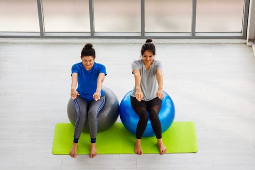 Above two Asian adult and young woman in sportswear doing aerobics yoga exercise with sitting on fitness ball indoor yoga studio, fit sport healthy workout lifestyle exercise