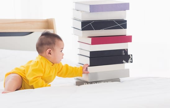 Asian cute baby little girl toddler looking at a stack of books on bedroom white bed, First baby library concept