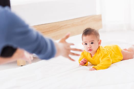 Asian happy young mother have fun learn walking crawling his daughter baby indoors bedroom at home. The mom playing with her little baby to crawl, two family