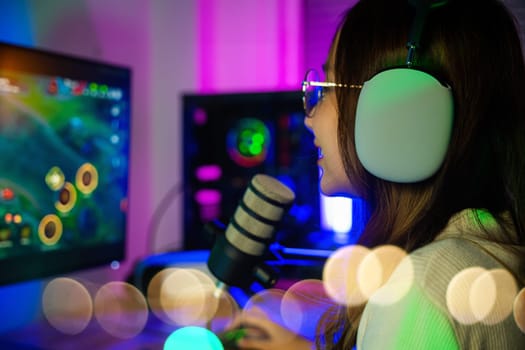 Asian young gamer woman playing video games online on computer she live stream and chat with fans, Happy streamer female talking with microphone in gaming room, game streaming concept