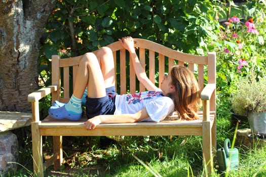 Blonde girl lies on a wooden Garden Bench.