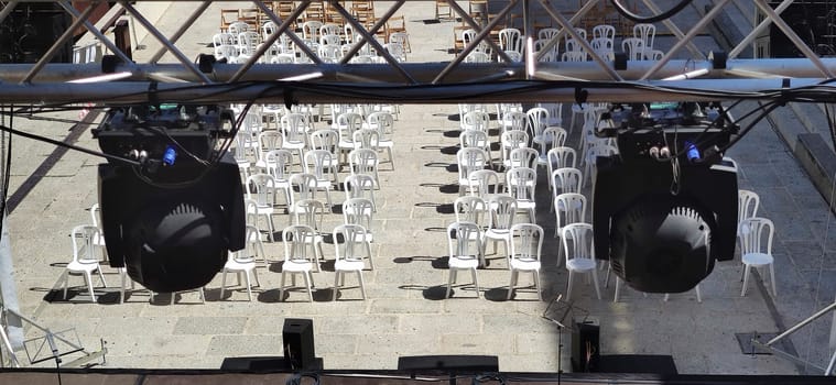 Spot lights structure over white plastic chairs for audience. Summer concerts in the city concept