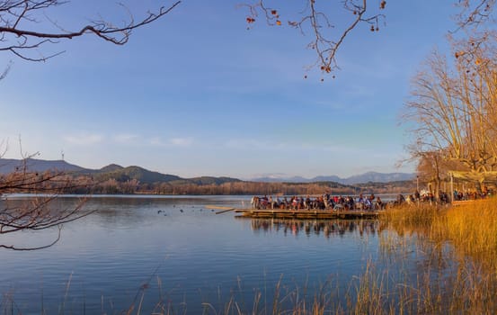 People enjoying the winter sun over pier restaurant at Lake of Banyoles, Girona, Catalonia, Spain