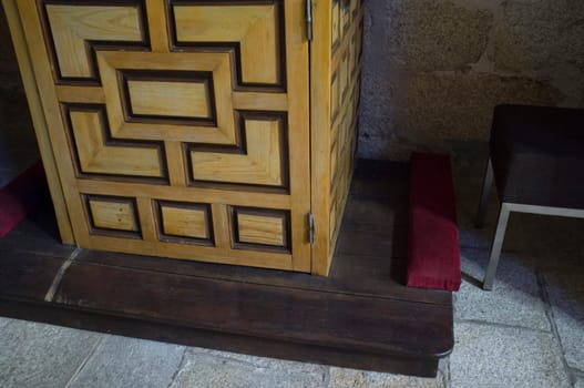 Wooden confessional foot with bench and prie-dieu cushion. Selective focus
