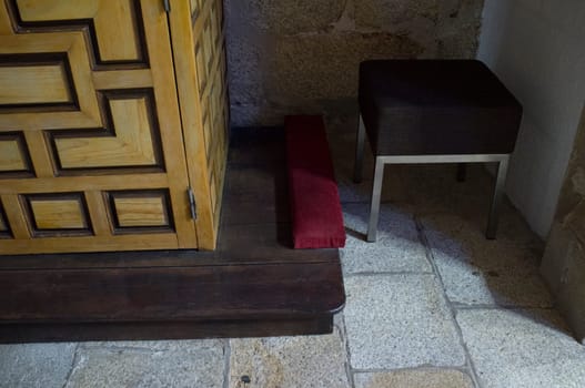 Wooden confessional foot with bench and prie-dieu cushion. Selective focus