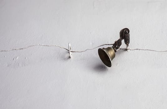Mechanically operated doorbell on a torsion spring actuated by a wire. Bell nailed to whitewashed wall