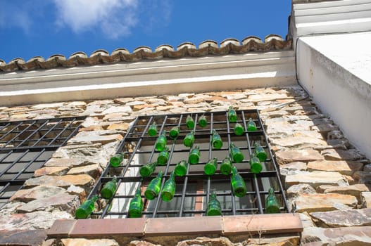 Rural residence house window decorared with hanging green glass bottles. Low angle view