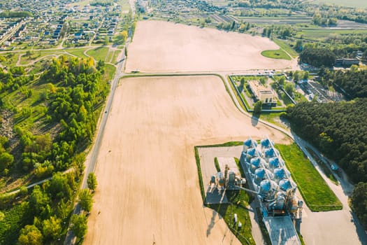 Aerial View Modern Granary, Grain-drying Complex, Commercial Grain Or Seed Silos In Sunny Spring Rural Landscape. Corn Dryer Silos, Inland Grain Terminal, Grain Elevators Standing In A Field.
