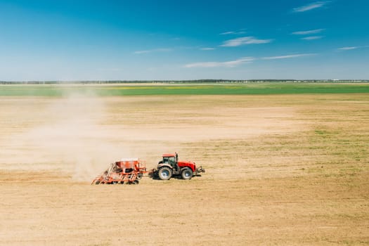 Aerial View. Tractor With Seed Drill Machine Sowing The Seeds For Crops In Spring Season. Beginning Of Agricultural Spring Season. Countryside Rural Field Landscape.