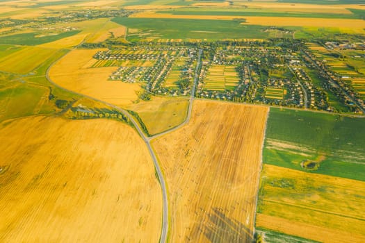 Aerial View Of Village And Hay Rolls, Straw Field Landscape In Summer Evening. Haystack, Hay Roll in Sunrise Time. Agricultural Countryside landscape In Harvest Season