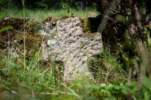 Very old single tombstone made of red sandstone overgrown with grass and weeds