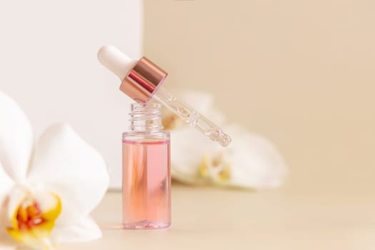 Light Pink opened Dropper Bottle with serum and a pipette near white orchid flowers on light beige, close up, copy space. Skincare cosmetic product, essence or serum. Everyday beauty routine.