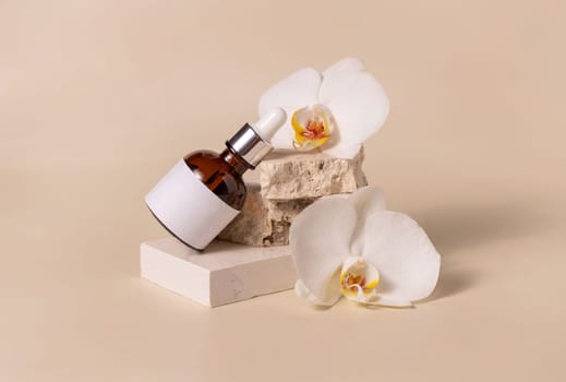 Brown glass dropper bottle with blank label laying on a stone near white orchid flowers on light beige, close up, mockup. Skincare beauty product, serum or essence. Exotic natural cosmetics..