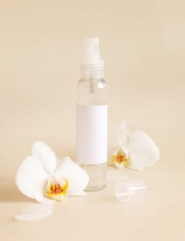 Spray dispenser bottle with blank label near white orchid flowers on light beige close up, cosmetic mockup. Skincare beauty product package. Exotic natural cosmetics, pastel minimal composition..