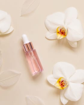Light Pink Dropper Bottle near white orchid flowers on light beige, top view, mockup. Skincare beauty product, Aromatic oil or serum. Exotic cosmetics, pastel minimal composition..
