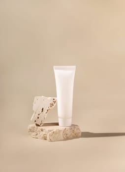 White plastic cream tube on travertine stone on light yellow, close up, mockup. Skincare beauty product. Natural cosmetics. Minimal composition..