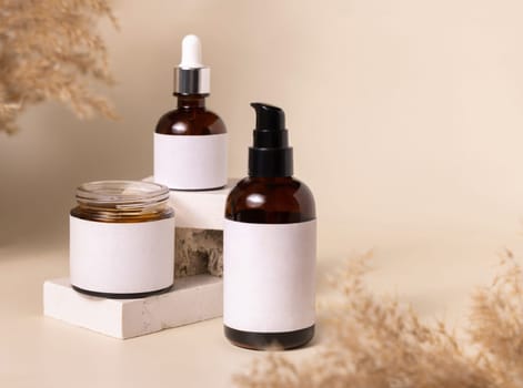 Cosmetic bottles on beige stones near dry pampas grass on light beige close up. Labels Mockup. Skincare beauty product packages. Natural cosmetics, minimal boho composition..