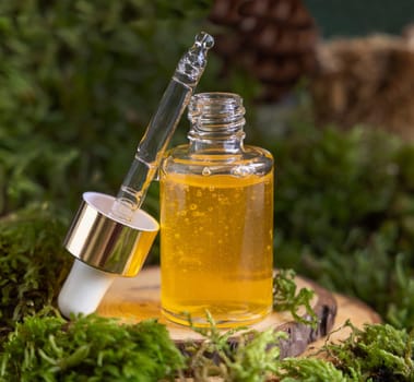Opened dropper bottle with yellow liquid near green moss, close up. Skincare beauty product, serum or essential oil, natural Organic Cosmetic concept