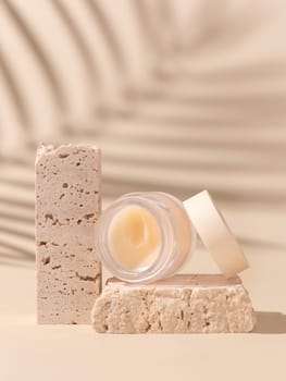 Smass Glass Cosmetic jar on travertine stones on light beige close up, palm leaf hard shadows. Skincare beauty product package. Exotic natural cosmetics, pastel minimal composition..