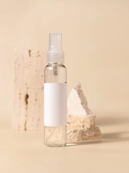 Spray bottle with blank label near stones on light beige close up, packaging mockup. Skincare beauty product, lotion or cleanser. Natural cosmetics, minimal composition..