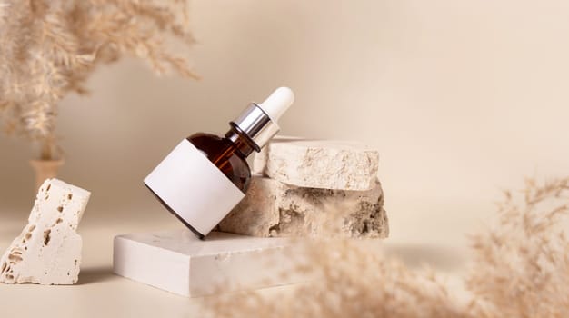 Brown dropper bottle with blank label on travertine stone near dry pampas grass on light yellow, close up, mockup. Skincare beauty product. Natural cosmetics. Boho composition..