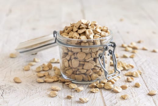 Glass jar of raw dry Grass pea on wood close up. Healthy, protein source for vegan and vegetarian diet. Traditional Italian apulian cuisine ingredient. Legumes known as Cicerchia, Vetch, Blue Sweet Pea