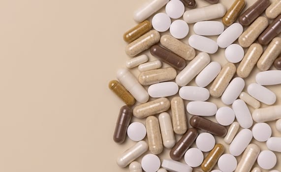 Mix of medical capsules and pills on light beige top view, copy space. Preventive medicine and healthcare, taking dietary supplements and vitamins. Assorted pharmaceutical medicine capsules