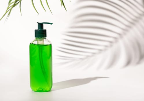 Refillable Cosmetic pump dispenser bottle filled with green liquid on white, Palm leaf hard shadows, close up, mockup. Skincare beauty product, facial cleaner or lotion. Natural cosmetics..